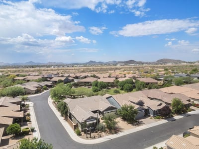 A panoramic aerial shot highlights the peaceful Phoenix neighborhood with mountain vistas, wide streets, and proximity to open desert terrain.