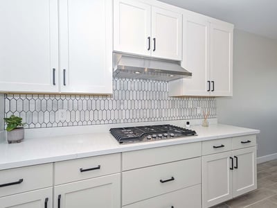A stunning combo of form and function with a built-in gas cooktop, vertical tile backsplash, and crisp white cabinetry designed for serious home chefs.