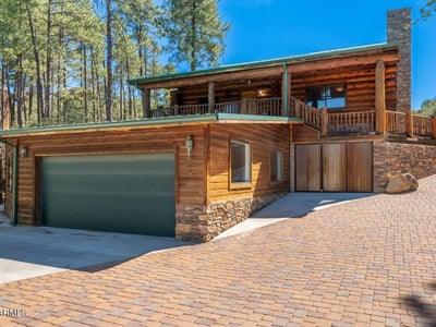 Eye-catching exterior featuring log siding, stone details, and a spacious driveway leading to a three-car garage. A welcoming first impression with timeless craftsmanship.