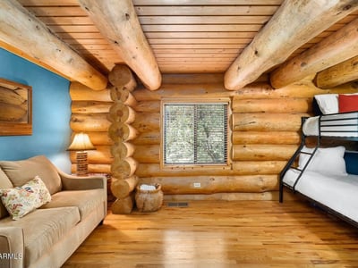 Multi-use bedroom with bunk beds, log walls, and hardwood flooring. Designed to accommodate guests while maintaining the authentic Prescott log home style.