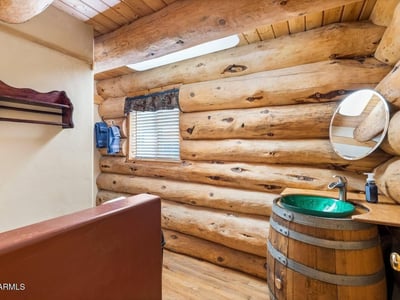 Distinctive bathroom with barrel vanity, vessel sink, log walls, and skylight adding character and natural light.