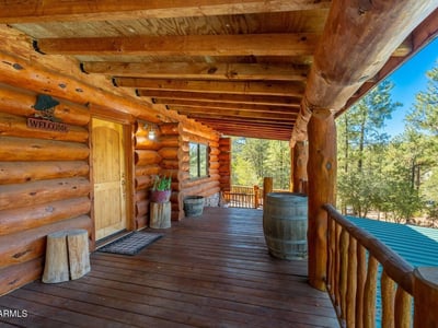 Covered front deck with log details and forest surroundings, setting the tone for this distinctive Prescott property.