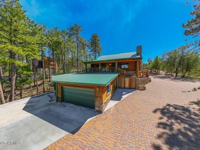 Wide paver driveway leading to a detached garage and covered entry. The stone chimney, metal roof, and wood exterior showcase craftsmanship and durability suited for Prescott s climate.