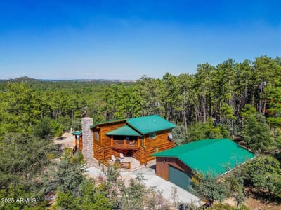 Aerial view showcasing the log home, detached garage, and surrounding trees. The durable metal roofing and natural materials reflect thoughtful design in this Prescott mountain setting.