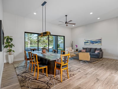 The dining space is framed by modern lighting and sliding doors, filling the room with views of the pool and golf course.