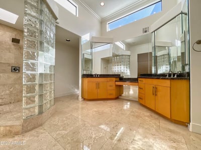 Spacious bathroom with high ceilings, glass-block shower, and granite vanities. Elegant design and natural light define this luxurious space.