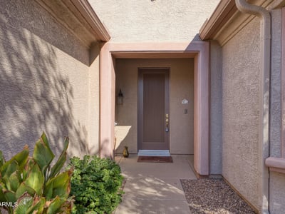 A covered entry framed by natural desert tones offers a warm welcome. Thoughtfully designed for shade and comfort, this entrance sets the tone for a peaceful home experience.