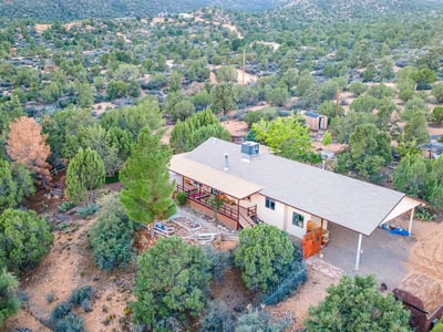 This elevated view highlights the wraparound deck, mature trees, and sprawling land. A serene retreat with endless possibilities for customization or self-sufficient living.