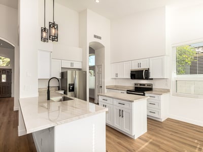 Updated Scottsdale kitchen featuring a spacious island, sleek quartz-style counters, white cabinetry, and stainless steel appliances. Modern pendant lighting and vaulted ceilings enhance the contemporary open layout.