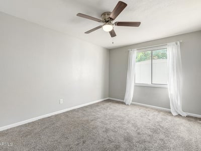 Bright primary bedroom with soft carpet, neutral finishes, and a ceiling fan an inviting retreat in this updated Phoenix home with a comfortable layout.