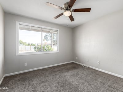 Spacious secondary bedroom with ceiling fan and soft carpeting perfect for guests or a dedicated workspace in this Phoenix property for sale.