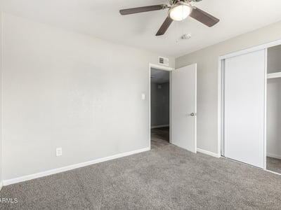 Secondary bedroom view showing plush carpet, bright window light, and closet storage move-in ready comfort in this Phoenix home.