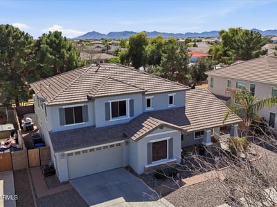 Elevated drone view showing the home's position within the neighborhood with distant mountain scenery and surrounding residential streets in Queen Creek.