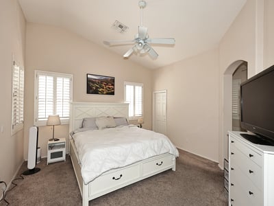 Primary bedroom with vaulted ceilings, ceiling fan, and plantation shutters. This Phoenix home offers a bright and airy space with neutral tones and plush carpet.