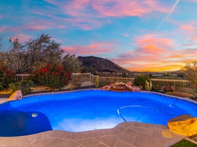 Scottsdale luxury pool illuminated at dusk with natural rock accents and sweeping mountain views, creating a serene and upscale backyard retreat.