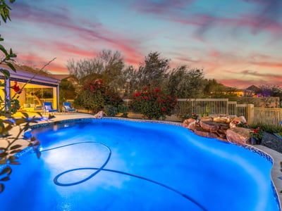 Scottsdale backyard with glowing pool, waterfall feature, and vibrant sunset backdrop, perfect for relaxing evenings outdoors.