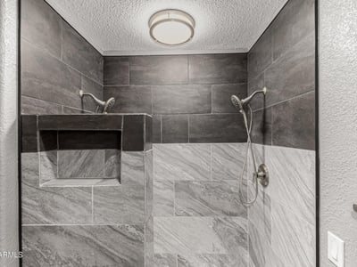 Walk-in shower featuring custom tile surround and built-in shelving. This Sun City home highlights upgraded bathrooms and contemporary style.