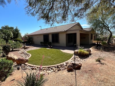 Beautiful backyard showcasing lush artificial turf, paver pathways, decorative rock features, mature desert plants, and tranquil golf course surroundings. A perfect outdoor retreat for relaxing or entertaining guests.