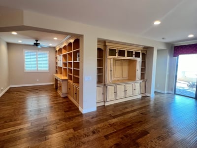 Open great room with stunning custom entertainment cabinetry, built-in office shelving, upgraded wood flooring, recessed lighting, and plantation shutters creating an elegant and highly functional living space.