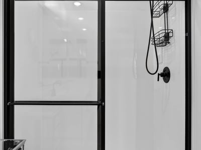 The oversized walk-in shower features sleek glass doors, contemporary black fixtures, built-in storage shelves, and a low-maintenance design that enhances the spa-like feel of the primary bath.