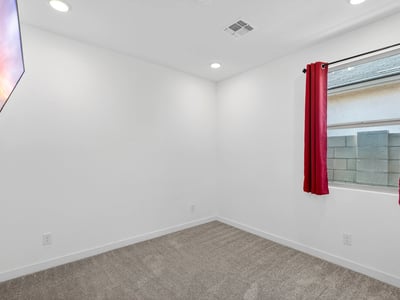 A bright guest bedroom with plush carpet, recessed lighting, and a large window provides comfortable accommodations while complementing the home's open and modern design.