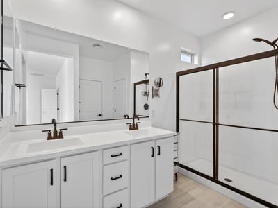 This well-appointed primary bathroom showcases dual sinks, quartz counters, modern cabinetry, black fixtures, and a spacious walk-in shower for a clean contemporary design.