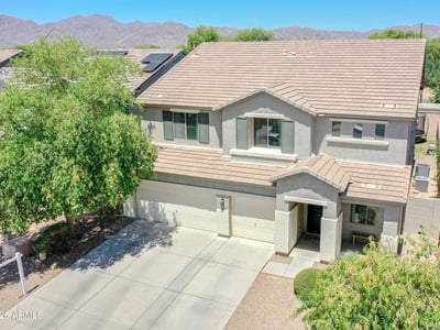 Elevated drone view highlighting the home's impressive exterior, expansive driveway, mature trees, and scenic mountain backdrop. A beautiful overview of this exceptional Waddell proper