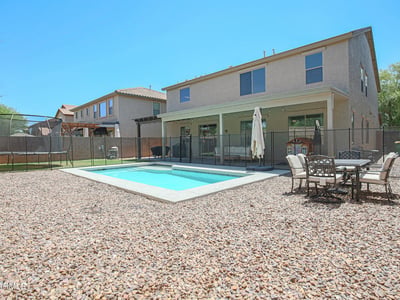 Wide backyard view highlighting the sparkling pool, covered patio, outdoor dining area, and generous outdoor space. A perfect setting for entertaining and enjoying life in Waddell.