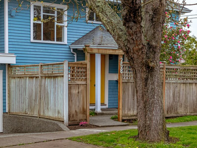 This inviting home features a unique yellow door, framed by a well-maintained wooden fence and inviting landscaping.