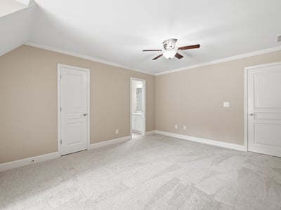 Spacious bedroom featuring soft carpeting, a ceiling fan, and access to a private bath.