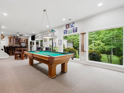 Spacious recreational room featuring a billiard table, large windows, and scenic views of the landscaped yard.