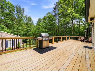 Spacious outdoor deck featuring a built-in grill, perfect for gatherings amidst lush greenery.