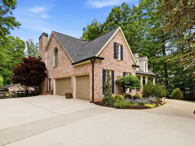 Stunning brick home with a spacious driveway, surrounded by lush landscaping and mature trees.