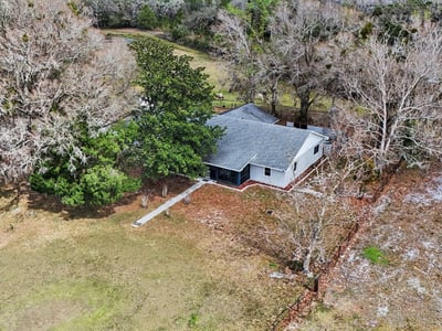 Aerial photo of the house with a front sidewalk as well as a rear entry sidewalk located off of the two car garage and paved slab parking area. This home is surrounded by mature trees and landscaping!