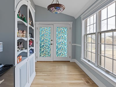 Bright and inviting sunroom with unique stained glass doors and built-in shelving for added character.