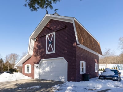 Unique barn-style home with ample space and convenient garage, set in a picturesque winter landscape.