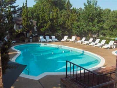 This property features a spacious outdoor pool area, surrounded by lush greenery and ample lounging options.
