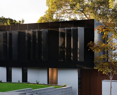 Modern architectural marvel featuring sleek black exterior and expansive windows, surrounded by lush greenery.