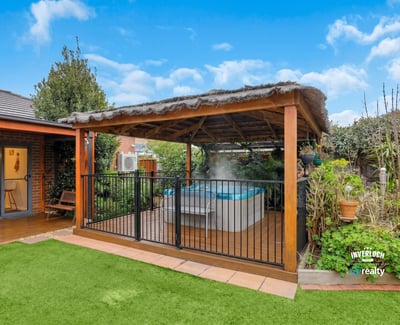 Discover a relaxing outdoor oasis featuring a covered patio and inviting hot tub surrounded by lush greenery.