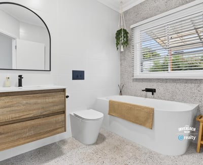 Modern bathroom featuring a freestanding tub, large mirror, and ample natural light from the window.