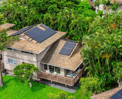Modern home featuring solar panels, nestled among lush tropical landscaping for sustainable living.