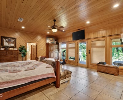Spacious master bedroom featuring wood accents, large windows, and direct access to outdoor greenery.