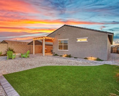 A twilight view showcases the home s well-planned backyard, featuring artificial turf, paver walkways, and accent lighting designed for beauty and efficiency in Litchfield Park.