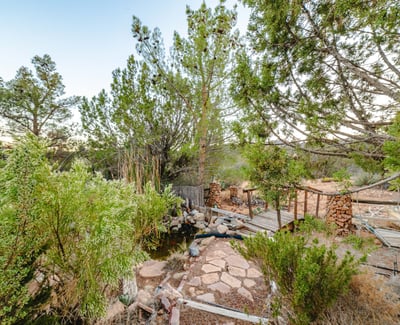 A charming footbridge crosses a small pond framed by natural stone and desert foliage. A picturesque highlight of this Hackberry acreage.