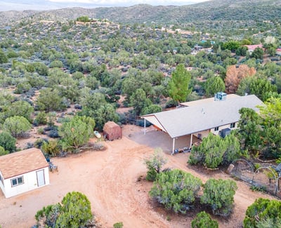 From above, the gated driveway and rugged terrain showcase the remote tranquility of this Hackberry homestead. The acreage invites exploration, gardening, and off-grid possibilities.