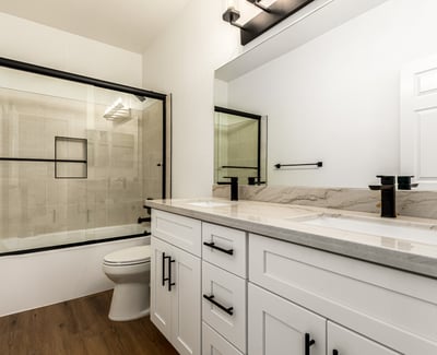 Updated Scottsdale guest bathroom with dual sinks, contemporary cabinetry, and modern black fixtures. The bathroom also includes a glass shower enclosure and elegant finishes that complement the home s remodeled interior.