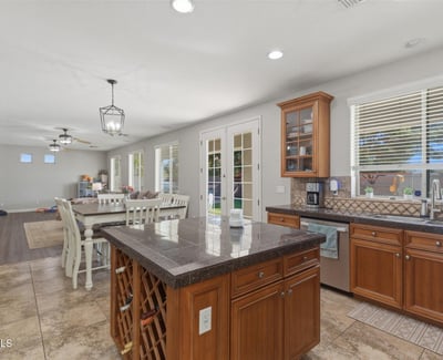 Bright kitchen with wood cabinetry, granite island, tile flooring, and large windows bringing in natural light from the backyard.