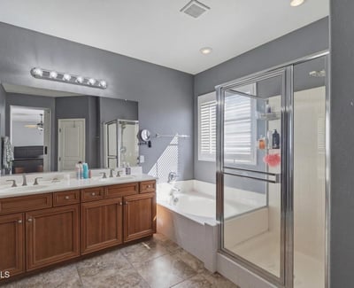 Primary bathroom with dual sinks, wood cabinetry, and bright lighting, providing a functional and stylish space for daily routines.