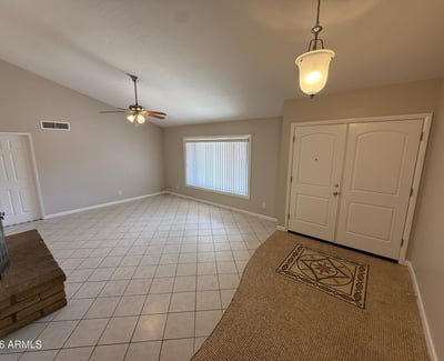 Spacious Glendale living room featuring tile flooring, neutral tones, vaulted ceilings, and a classic stone fireplace. The open design provides a comfortable gathering space with plenty of natural light.