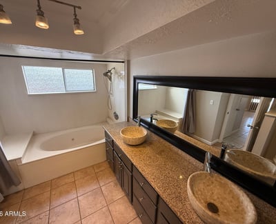 Primary bathroom featuring granite countertops, dual vessel sinks, and large mirror for added functionality. Tile flooring and warm finishes create a comfortable and practical bathroom space.